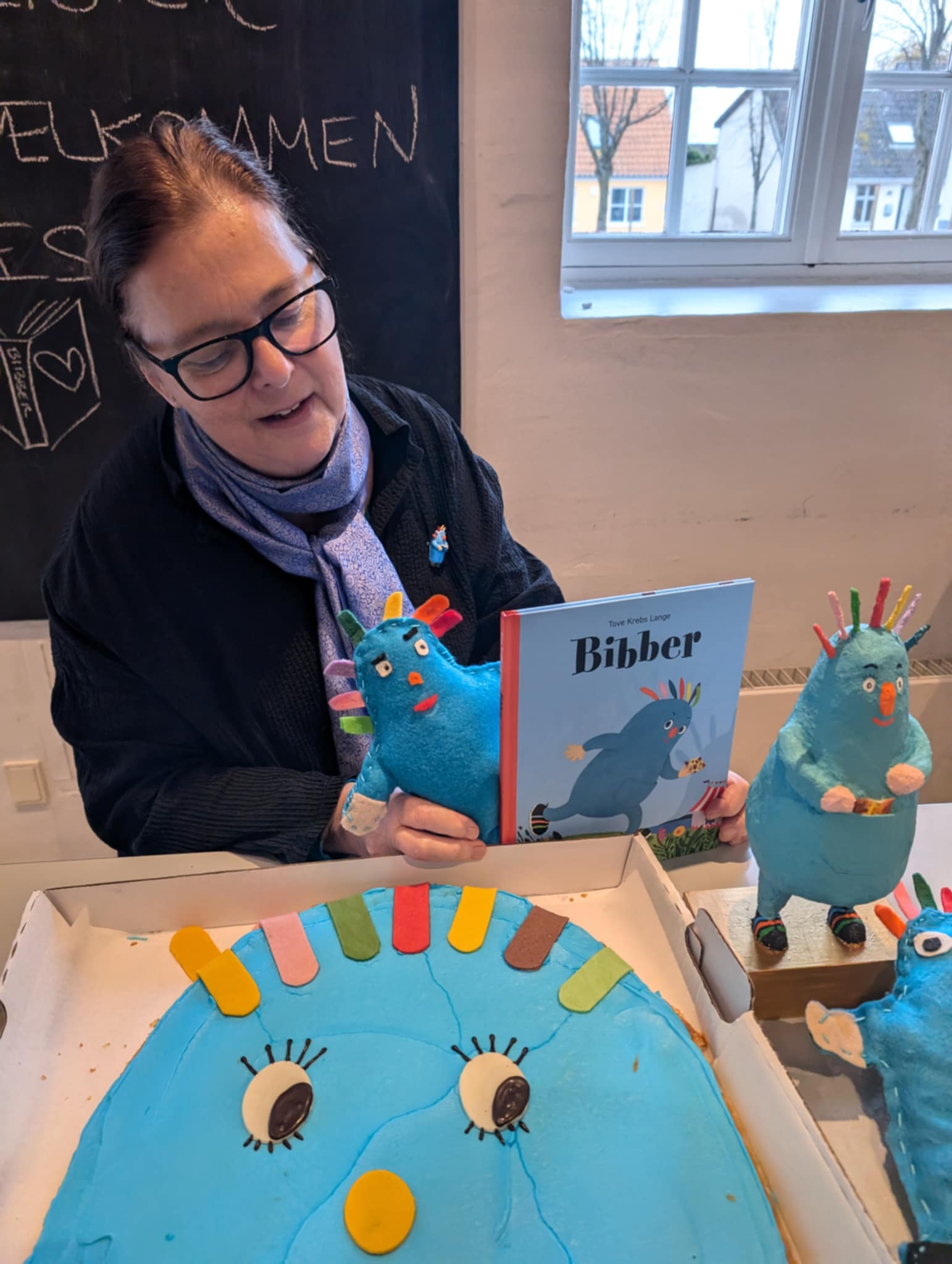 Tove Krebs Lange omgivet af Bibbere lavet i papmaché, filt, kage og Bibber-bogen